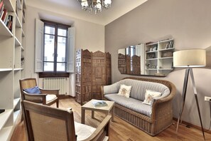 Ein Wohnzimmer mit einer Couch, Sesseln, einem Couchtisch, einem Bücherregal, einem Spiegel und einer Stehlampe.