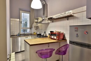 Eine kleine Küche mit Herd, Toaster und Kühlschrank, einer Holzarbeitsplatte und zwei violetten Barhocker.