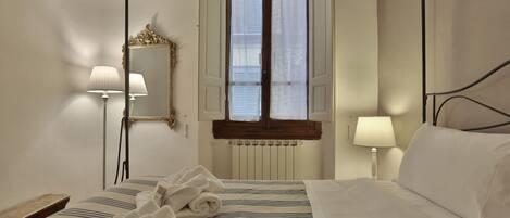 A hotel room with a four-poster bed, two bedside lamps, a mirror, a window with shutters, and a radiator.