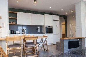 Eine moderne Küche mit weißen Schränken, einem Holztisch und einem integrierten Fernseher.