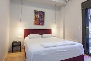 Ein ordentlich bezogenes Bett mit weißen Leinen, einem roten Kopfteil und zwei Pendelleuchten.