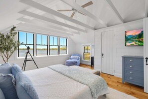 A bedroom with a large bed, a chair, a desk, and a painting on the wall.