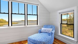 A room with a large window, a blue patterned chair, and a pillow with 'Coastal Life' text. - Edgewater Sanctuary | Fully Off Grid Ocean Cottage | Directly on Buzzard's Bay (Wareham)