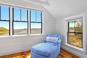 A room with a large window, a blue patterned chair, and a pillow with 'Coastal Life' text.