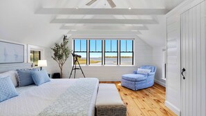 A bedroom with a large bed, a chair, a window with a view, and a ceiling fan. - Edgewater Sanctuary | Fully Off Grid Ocean Cottage | Directly on Buzzard's Bay (Wareham)