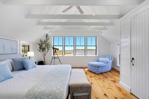 A bedroom with a large bed, a chair, a window with a view, and a ceiling fan.
