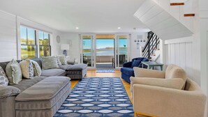 A spacious living area with a large sofa set, a patterned rug, and a view through glass doors to an outdoor patio. - Edgewater Sanctuary | Fully Off Grid Ocean Cottage | Directly on Buzzard's Bay (Wareham)