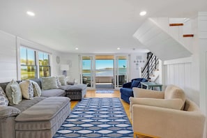 A spacious living area with a large sofa set, a patterned rug, and a view through glass doors to an outdoor patio.