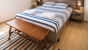 A bedroom with a wooden bed, a bedside table, a nightstand, a bench, and a wall-mounted picture. - Cocoon apartment in Sanguinet - lake, forest, Pilat dune and ocean (Sanguinet)