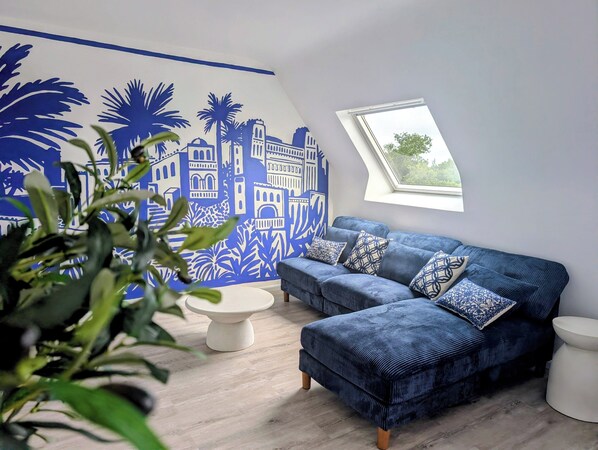 Una sala de estar moderna con un sofá azul, una mesa de centro blanca y un mural con diseños arquitectónicos.