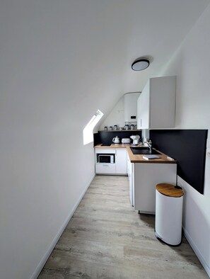 Una cocina moderna y estrecha con encimera de madera, armarios blancos y un pequeño cubo de basura.