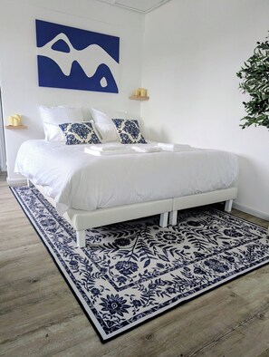Un lit bien fait, avec une literie blanche et des coussins à motifs bleus, un tapis à motifs floraux bleus et blancs, et une peinture abstraite bleue accrochée au mur.