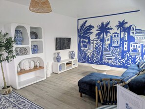 Un salon moderne aux couleurs bleu et blanc, comprenant un canapé, un téléviseur et des objets décoratifs disposés sur des étagères.