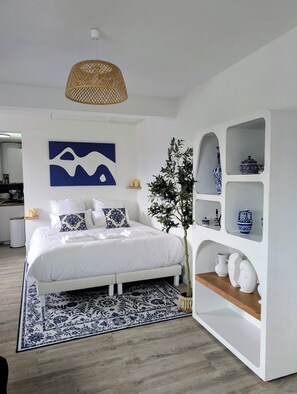 Un dormitorio moderno con una cama grande, una lámpara colgante de ratán, un estante de pared con objetos decorativos y una alfombra de estampado azul y blanco.