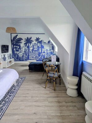 Une chambre avec un plafond en pente, un lit, une chaise, une table et une fresque murale.
