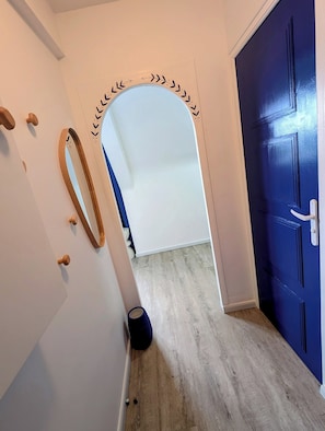 Un couloir avec une porte bleue, un mur blanc orné d’une arche décorative et un plancher en bois.