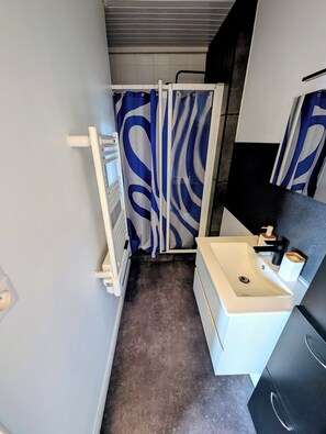 Une salle de bain avec un lavabo blanc, un robinet noir et un miroir. On y trouve également une douche avec un rideau de douche bleu et blanc.