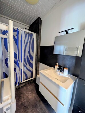 Un baño con lavamanos blanco, espejo y cortina de ducha con estampado azul y blanco.