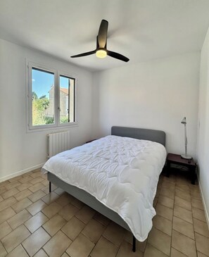 A bedroom with a bed, a ceiling fan, a window, and a radiator. - Vrbo Property (Arles)