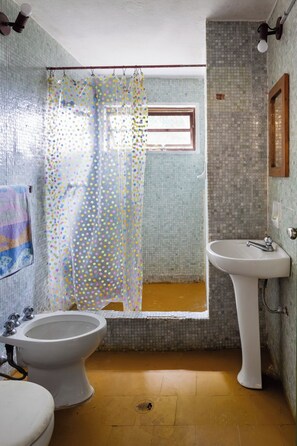 Un baño con cortina de ducha, un lavabo y dos inodoros.