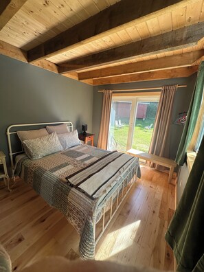 A bedroom with a wooden bed, a bedside table, a bench, and a window with curtains.