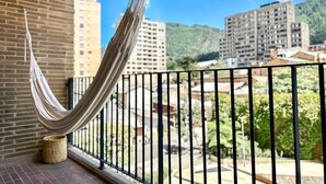 Un balcón con una hamaca, un muro de ladrillo y vistas a edificios y vegetación.