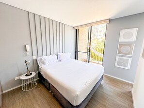 A modern bedroom with a bed, a bedside table, a lamp, and a window with a view of buildings. - Prime District 1302 (Bogotá)