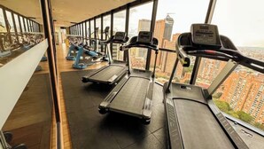 Un gimnasio con cintas de correr y bicicletas estáticas, amplias ventanas con vista a la ciudad.