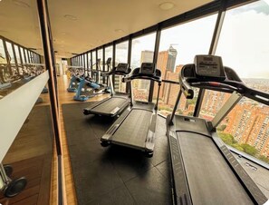 Ein Fitnessstudio mit Laufbändern und Ergometer, große Fenster mit Blick auf die Stadt.