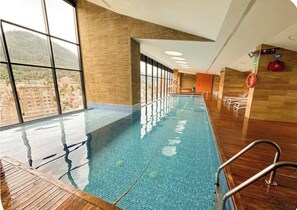 An indoor swimming pool with clear glass walls, wooden flooring, and a view of buildings outside. - Prime District 1302 (Bogotá)