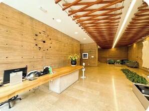 A reception area with a wooden reception desk, a clock on the wall, and a seating area with a sofa and chairs. - Prime District 1302 (Bogotá)