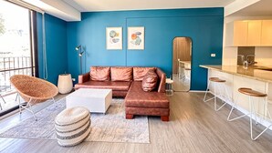 Una sala moderna con sofá, mesa de centro y otomanas, una cocina con taburetes de bar y obras de arte en las paredes.