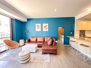 Ein modernes Wohnzimmer mit Sofa, Couchtisch und Hocker, eine Küche mit Barhocker und Kunstwerken an den Wänden.