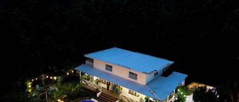Une grande maison avec une piscine, entourée d’une végétation luxuriante et offrant une vue sur les montagnes lointaines.
