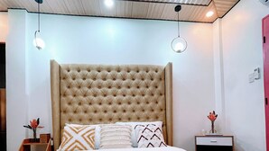 Ein Schlafzimmer mit einem karopolierten Kopfteil, einem Bett mit weißer Bettwäsche, mehreren Kissen, Nachttischen mit Lampen und einem roten Kissen mit Muster.