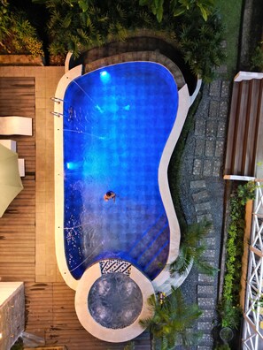 Una piscina de borde curvo, rodeada por un sendero de piedra y follaje.