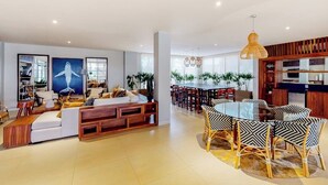A modern living room with a sofa, dining table, and chairs, a kitchen area, and a large window. - Exquisite Apartment With Balcony, TV, Wifi, Heated Pool & Gym/fitness Room (Cabo San Lucas)