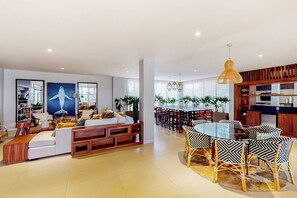 Ein modernes Wohnzimmer mit einer Couch, einem Esstisch, Stühlen, einer Küchenzeile und einem großen Fenster.