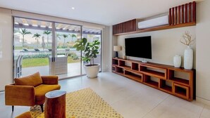 A modern living room with a TV, sofa, and potted plant. - Exquisite Apartment With Balcony, TV, Wifi, Heated Pool & Gym/fitness Room (Cabo San Lucas)