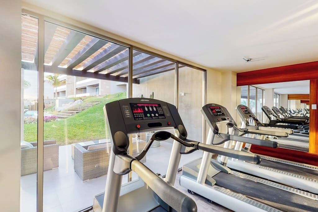 A gym with treadmills and exercise equipment, large windows, and a view of a building and greenery.