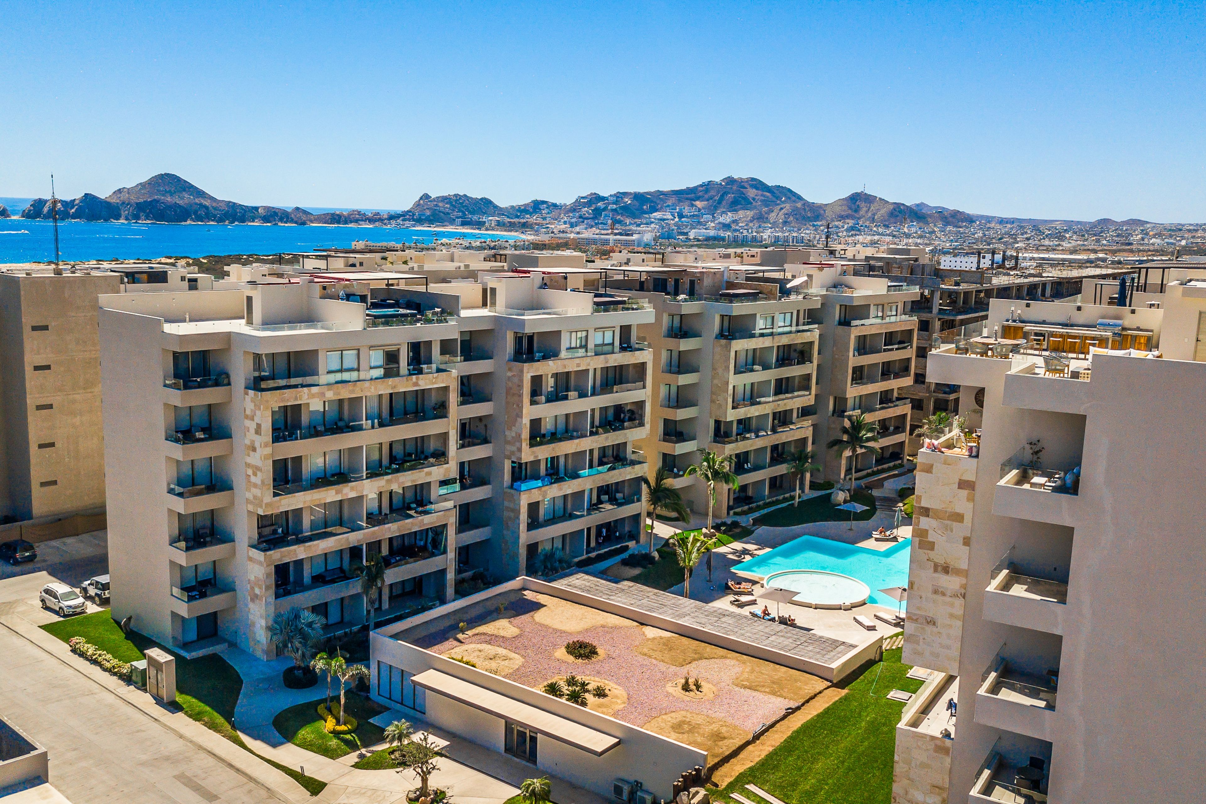 A multi-story hotel with a rooftop pool, surrounded by other buildings and a mountain in the background.