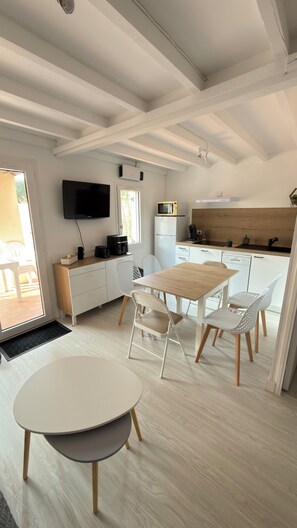 Una cocina moderna con comedor, muebles blancos, un televisor de pantalla plana y una mesa de comedor de madera.