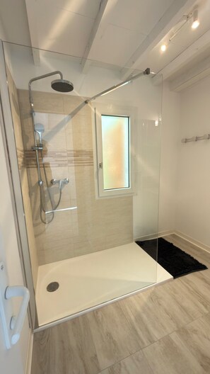 Una ducha moderna con cerramiento de vidrio, una ventana pequeña y suelo de madera.