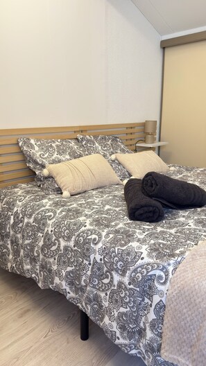 Een net opgemaakt bed met patroonlinnen, een houten hoofdbord en een nachtkastje met een lamp.