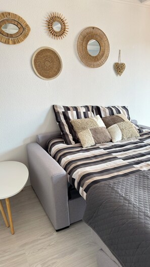 Un dormitorio moderno con un sofá gris, un edredón a rayas y espejos decorativos en la pared.