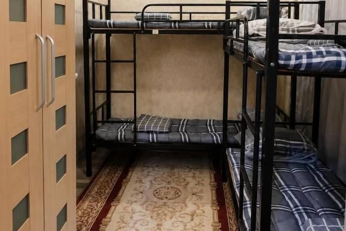 A bunk bed room with a patterned rug, wooden wardrobe with glass panels, and a plain wall.