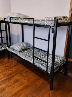 A bunk bed with a checkered mattress and pillows, a wooden floor, and a plain wall. - Ayvan Eco Hostel (Tashkent)