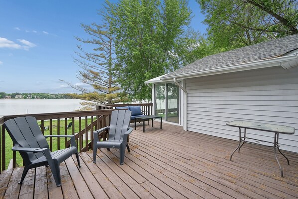 A wooden deck with Adirondack chairs and a table, overlooking a body of water and trees. - Lakefront 2 bedroom house in Zimmerman on Elk Lake (Zimmerman)