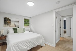 A bedroom with a bed, a nightstand, a window, and a door leading to another room. - Lakefront 2 bedroom house in Zimmerman on Elk Lake (Zimmerman)