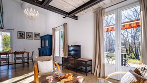 A spacious living room with a dining area, a television, and a large window with curtains. - House in Villars, in the ochre hills of the Luberon, Vaucluse (Villars)